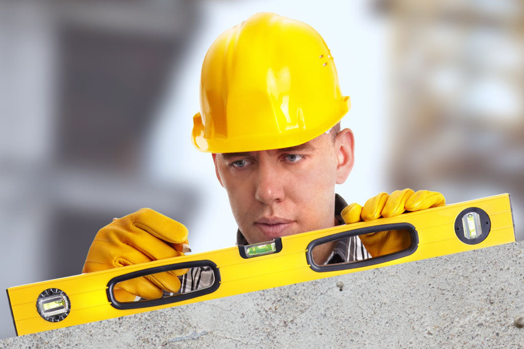 Rakennustyöntekijä tarkistamassa vesivaa'alla betonipinnan suoruutta.