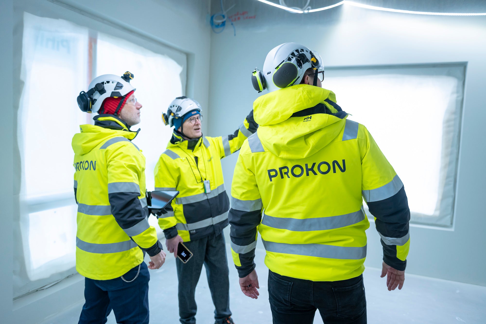 Kolme HT-Prokonin työntekijää huomioliiveissä keskustelemassa rakennustyömaan sisätiloissa.