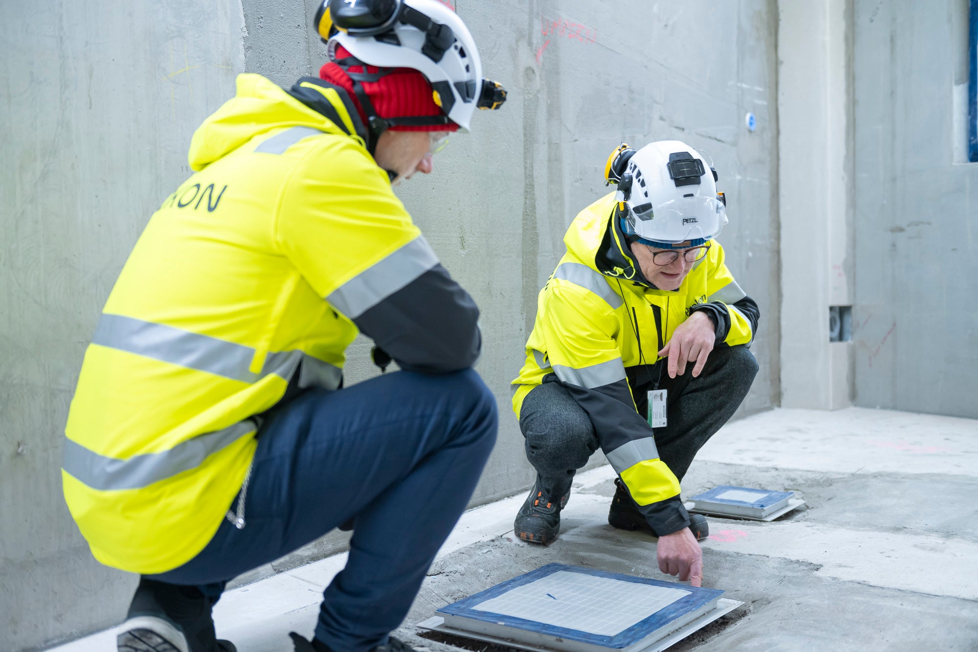 Kaksi HT-Prokonin työntekijää tarkastamassa lattian tarkastusluukkua betonisessa kellaritilassa.