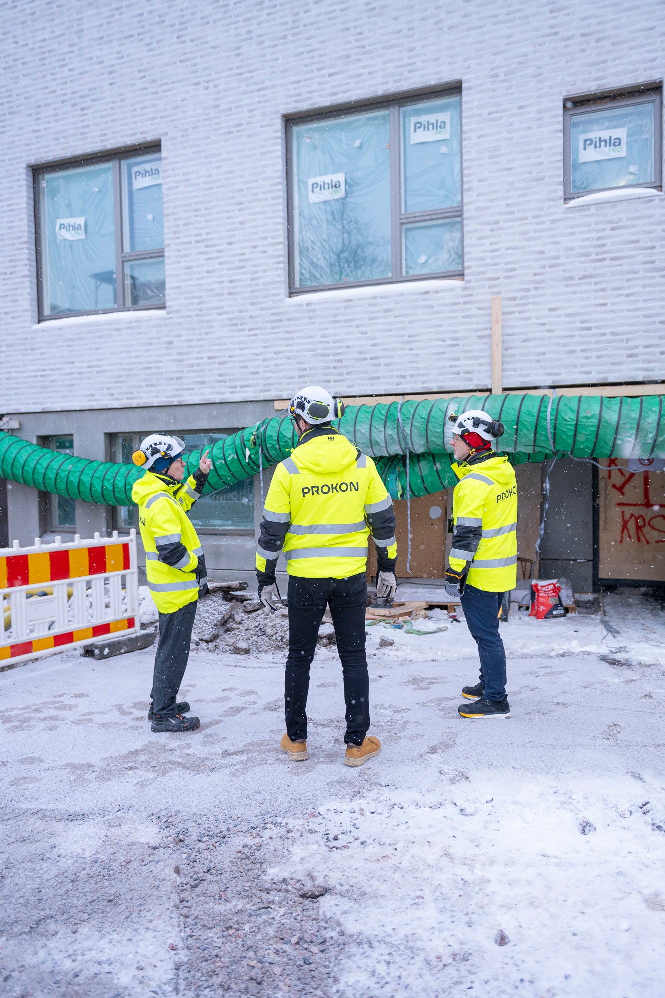 Kolme HT-Prokonin työntekijää huomioliiveissä keskustelemassa rakennustyömaalla lumisateessa.